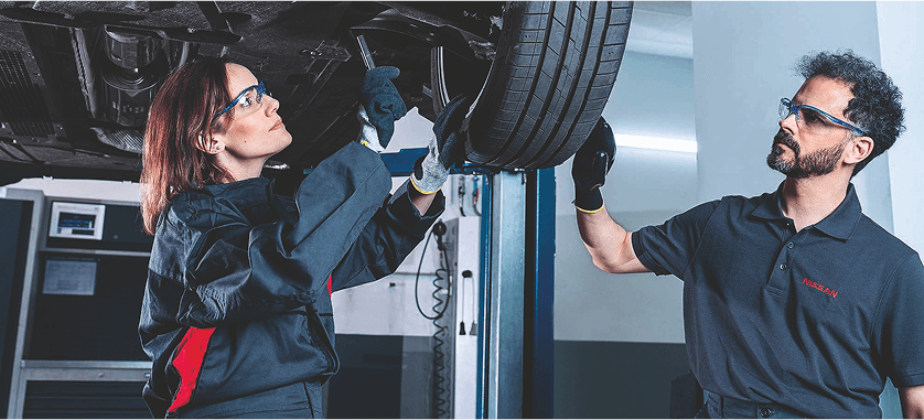 Zwei Mechaniker prüfen ein angehobenes Auto am Rad.